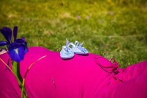 Pregnant woman lying on a grass with baby shoes on her belly photo