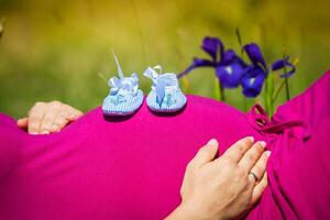 Pregnant woman lying on a grass with baby shoes on her belly photo