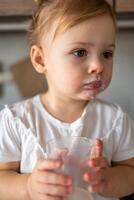 Happy baby girl sitting at the table in the kitchen and drinking milk photo