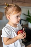 Baby girl blonde eating an apple in the kitchen, concept of healthy food for children photo