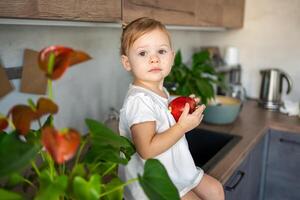 Baby girl blonde eating an apple in the kitchen, concept of healthy food for children photo