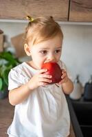 Baby girl blonde eating an apple in the kitchen, concept of healthy food for children photo