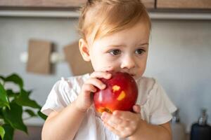 Baby girl blonde eating an apple in the kitchen, concept of healthy food for children photo