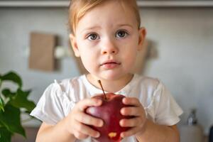 Baby girl blonde eating an apple in the kitchen, concept of healthy food for children photo