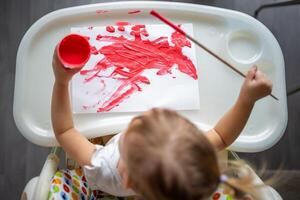 linda pequeño niña pintura con cepillos a hogar. creativo juegos para niños. permanecer a hogar entretenimiento foto