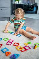 pequeño niña jugando vistoso imán el plastico bloques equipo a hogar. el niño jugando educativo juegos. temprano infancia desarrollo. foto