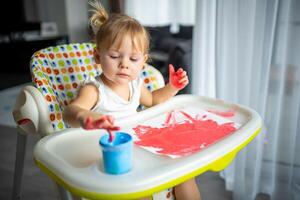 linda pequeño niña pintura con dedos a hogar. creativo juegos para niños. permanecer a hogar entretenimiento foto