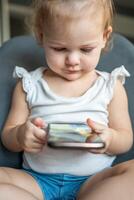 Smiling little girl is sitting on armchair and using smart phone photo