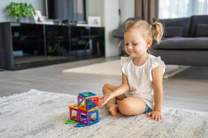 Little girl playing colorful magnet plastic blocks kit at home. The child playing educational games. Early childhood development. photo