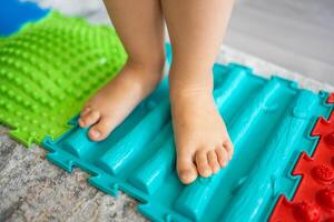 Close up view of Little girl walks on a massage mat. Toddler baby foot massage mat. Exercises for legs orthopedic massage carpet. photo