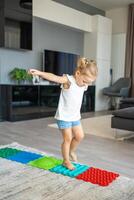 pequeño niña camina en un masaje estera. niñito bebé pie masaje estera. ejercicios para piernas ortopédico masaje alfombra. foto