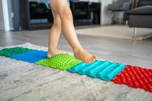 Close up view of Little girl walks on a massage mat. Toddler baby foot massage mat. Exercises for legs orthopedic massage carpet. photo