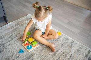 Cute caucasian little girl playing on the floor at home with eco wooden toys. Montessori toy. The child playing educational games. photo