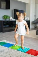 pequeño niña camina en un masaje estera. niñito bebé pie masaje estera. ejercicios para piernas ortopédico masaje alfombra. foto