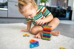 pequeño niña jugando vistoso imán el plastico bloques equipo a hogar. el niño jugando educativo juegos. temprano infancia desarrollo. foto