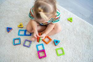 pequeño niña jugando vistoso imán el plastico bloques equipo a hogar. el niño jugando educativo juegos. temprano infancia desarrollo. foto