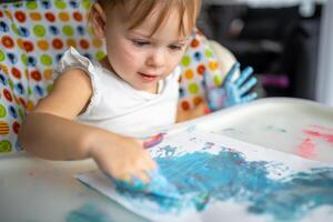 Cute little girl painting with fingers at home. Creative games for kids. Stay at home entertainment photo