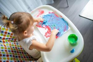 Cute little girl painting with fingers at home. Creative games for kids. Stay at home entertainment photo