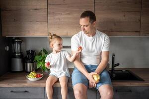 linda pequeño niña y su hermoso papá son comiendo Fruta en moderno cocina. sano comiendo. foto