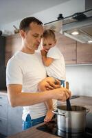 Father with his daughter on his hands cooking soup together in modern home kitchen photo