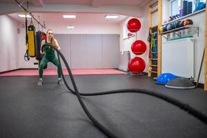 Young woman with perfect body doing crossfit exercises with a rope in the gym. photo
