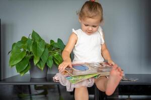 adorable niñito pequeño niña leyendo libro a hogar. felicidad niño leyendo libro para preescolar disfrutar con aprendizaje educación por tú mismo. educación concepto foto