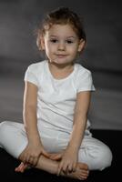 Little cute girl practicing yoga pose on grey background in dark room photo