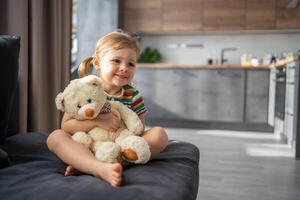 Cute little girl hugging teddy bear while sitting on sofa at home photo