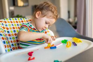 pequeño niña obras de teatro con multicolor arcilla de moldear, crea diferente formas foto