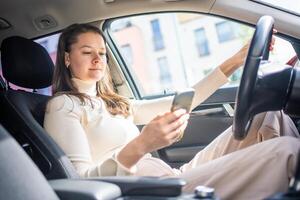 Young woman sitting in car and using smart phone, business woman busy driving photo