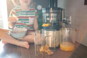 Little girl making fresh juice on the table in home kitchen. Focus on juicer photo