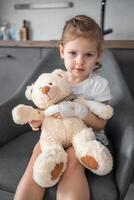 Little girl with broken finger holds teddy bear with a bandaged paw at the doctor's appointment in the hospital photo