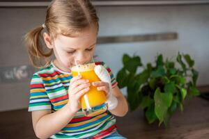 Little girl drinking fresh juice sitting on table in home kitchen photo