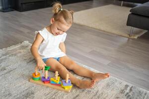 linda caucásico pequeño niña jugando en el piso a hogar con eco de madera juguetes montessori juguete. el niño jugando educativo juegos. foto