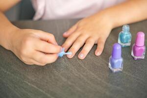 Top view of Hands of little girl doing manicure and painting nails with colorful pink, blue and purple nail polish at home photo