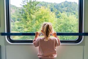 Beautiful little girl looking out train window outside, while it moving. Traveling by railway in Europe photo