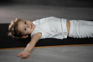 pequeño niña relajarse y meditar acostado en el estera mientras practicando yoga en oscuro habitación foto