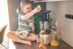 Little girl making fresh juice sitting on the table in home kitchen photo