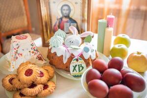 Pascua de Resurrección pastel con pintado huevos, manzanas y galletas en mesa en hogar cocina. Iglesia íconos y vela en antecedentes. ortodoxo religión tema. foto