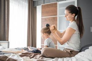 Young mother combs her little daughter's hair while sitting in bed in the morning photo