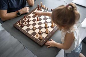 padre enseñando su pequeño hija a jugar ajedrez a el mesa en hogar cocina. el concepto temprano infancia desarrollo y educación. familia ocio, comunicación y recreación. foto