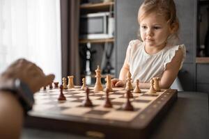 padre enseñando su pequeño hija a jugar ajedrez a el mesa en hogar cocina. el concepto temprano infancia desarrollo y educación. familia ocio, comunicación y recreación. foto