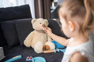 Little girl playing doctor with toys and teddy bear on the sofa in living room at home photo