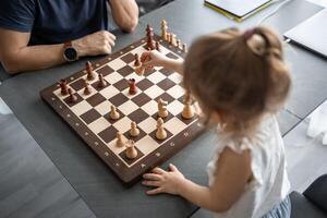 Little girl playing chess with her father at the table in home kitchen. The concept early childhood development and education. Family leisure, communication and recreation. photo