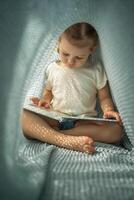 pequeño niña disfrutando de revisión un libro debajo azul de punto tartán en soleado Mañana foto