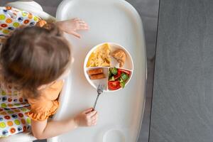 pequeño niña tener un equilibrado desayuno en hogar cocina en el Mañana foto