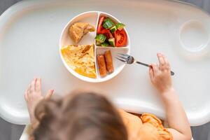 pequeño niña tener un equilibrado desayuno en hogar cocina en el Mañana foto