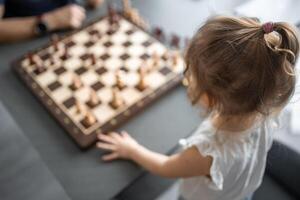 Father teaching his little daughter to play chess at the table in home kitchen. The concept early childhood development and education. Family leisure, communication and recreation. photo