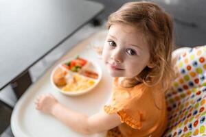 pequeño niña tener un equilibrado desayuno en hogar cocina en el Mañana foto
