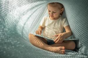 Little girl enjoying of review a book under blue knitted plaid in sunny morning photo